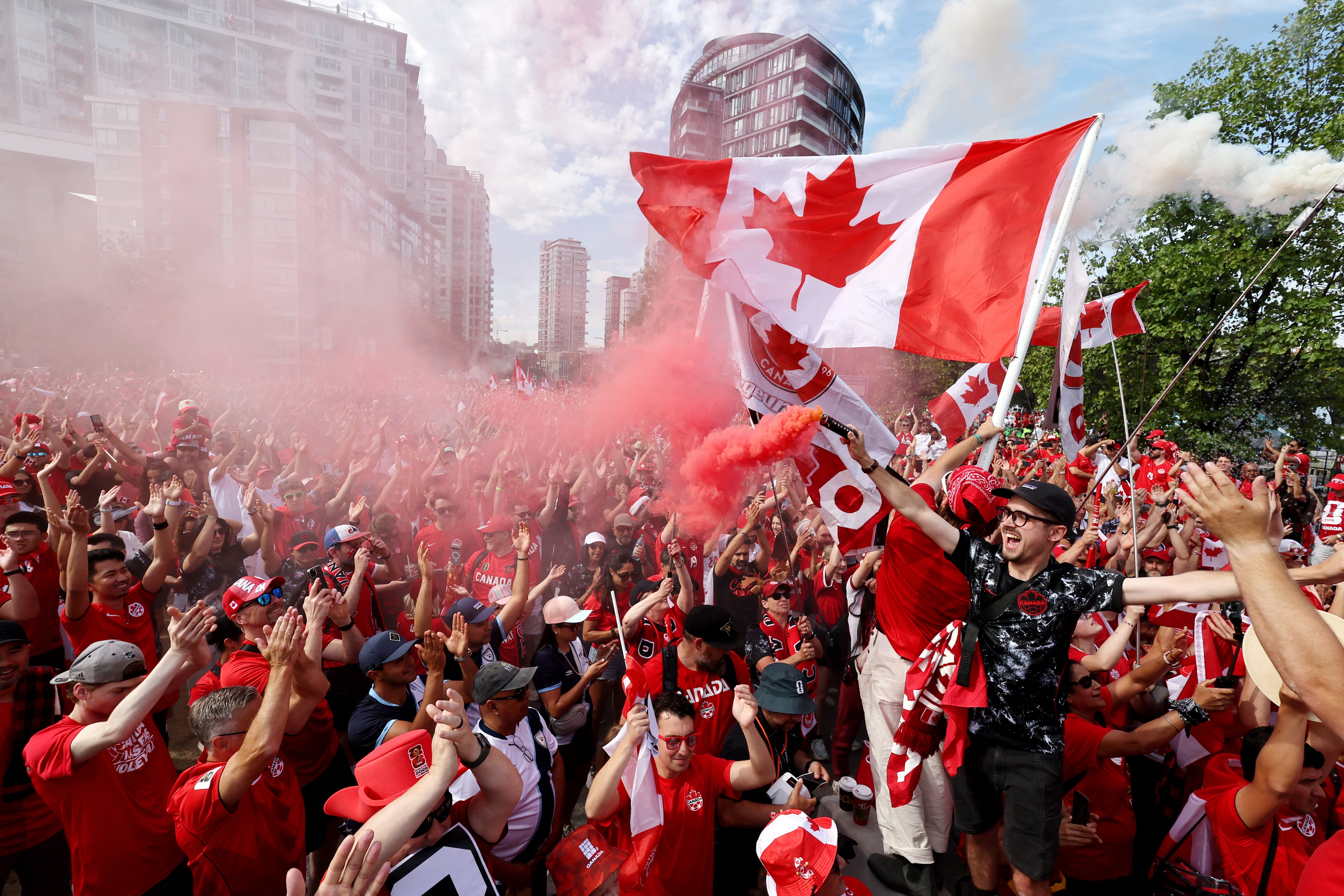 Canadian football fans celebrating on a city street with flags, scarves, and World Cup screens in the background